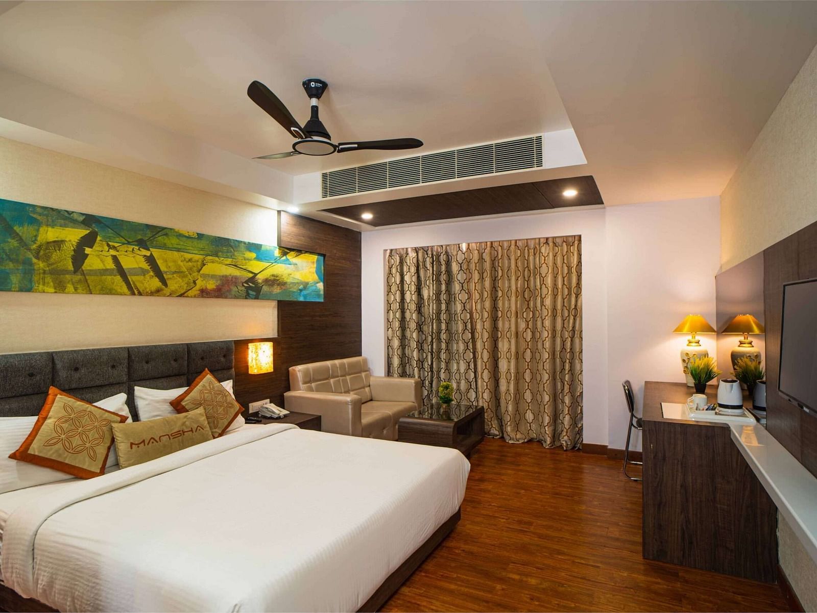 A room with a bed, a sofa, a wall-mounted television, and a ceiling fan at Mansha Hotel Regency.