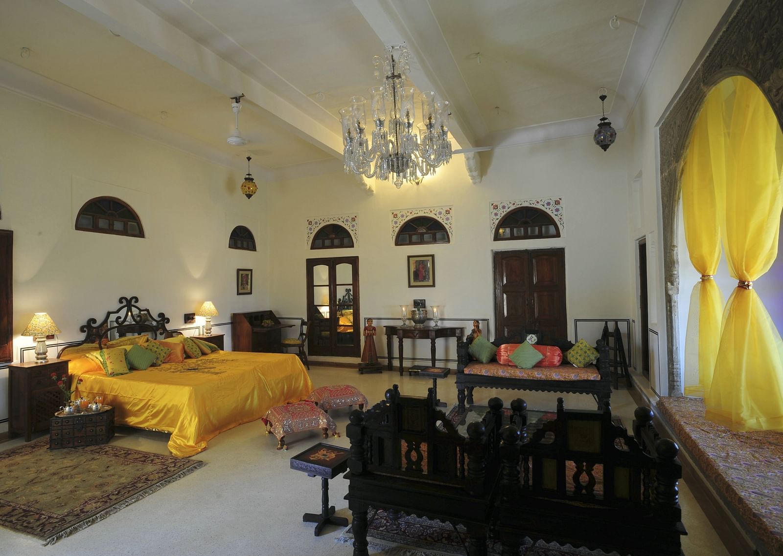 A spacious suite at Fort Barli, Ajmer, includes a bed, seating areas, a chandelier, and draped windows.