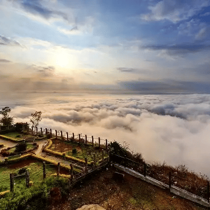 A panoramic shot of Nandi Hills in Bengaluru featuring amnucured garden overlooking a cloud covered landscape.