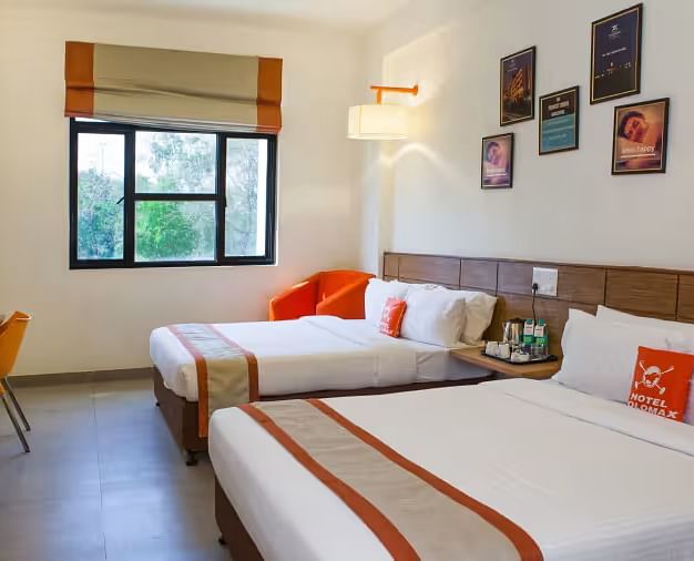View of a hotel room featuring two comfortable beds, wall art, and a large window with natural light - Max Hotel Prayagraj.