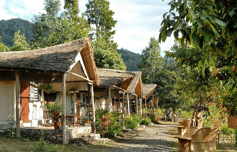 The Jamoon Resort in Jim Corbett National Park featuring individual huts, surrounded by trees and mountains.