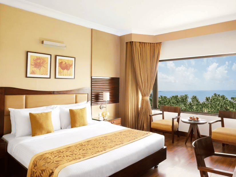 A king sized bed in a bedroom at The Retreat Hotel & Convention Centre with a picturesque view,  a desk and chair, two chairs, a tea table and bedside table.