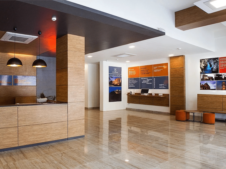alt-text A spacious and modern hotel reception with a seating area, polished stone floors, and posters providing local information and attractions.