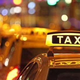 close up image of the taxi signage glowing during the night put above yellow coloured taxis