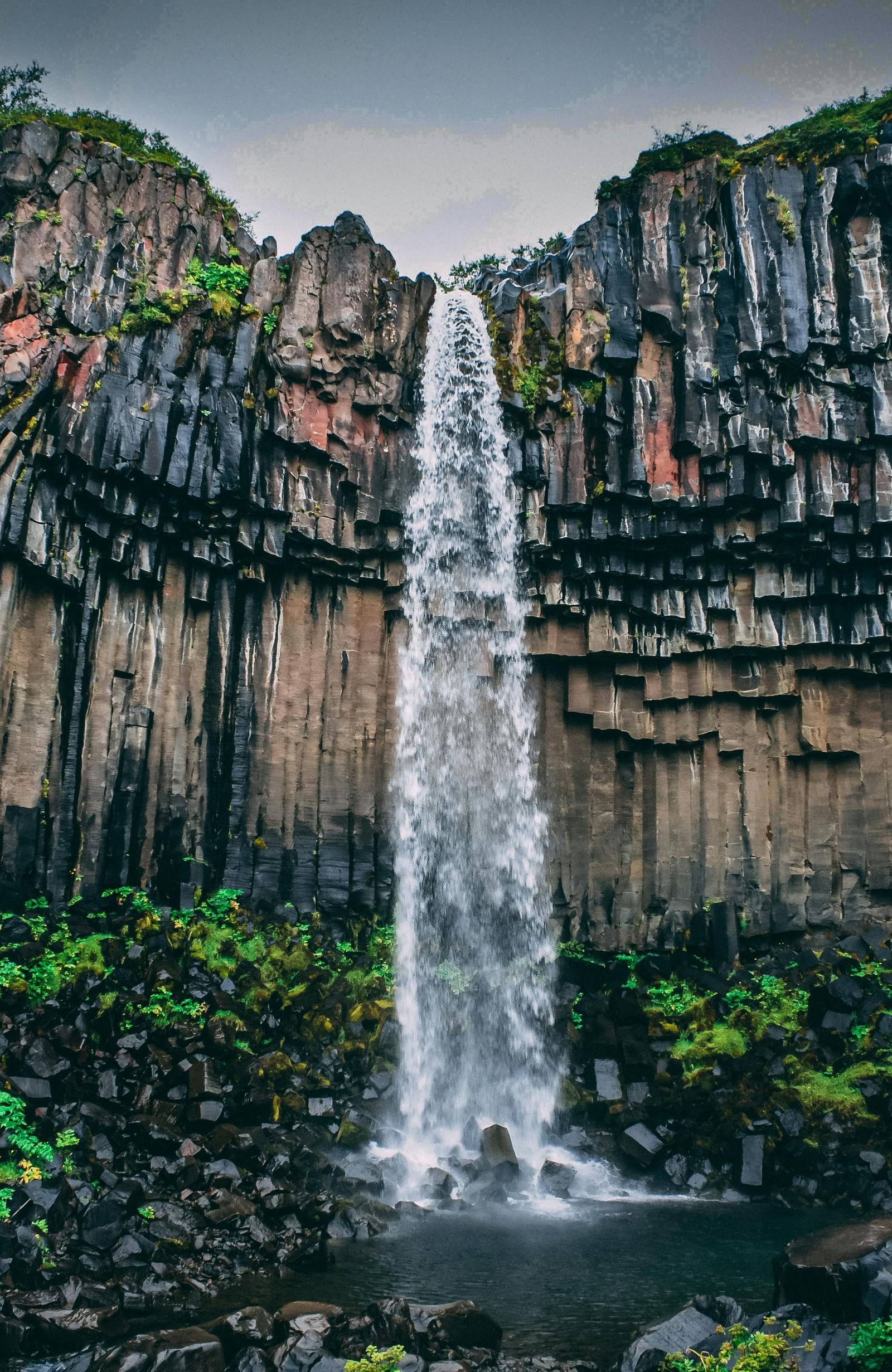 A view of a waterfall surrounded by greenery on an overcast day