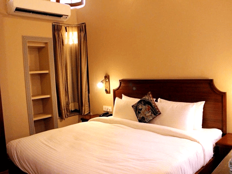 A room with a large bed, spreads, pillows, and lights. | Hotel Devnadi, Haridwar