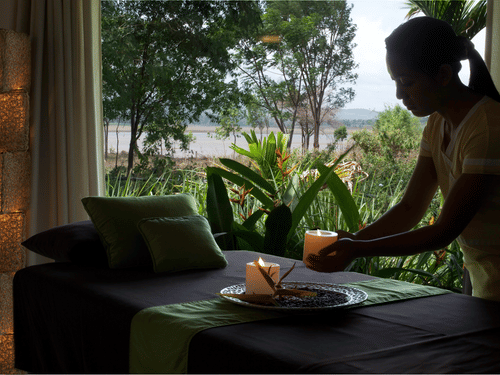A person putting candles on a table in a semi-dark room in front of a window with the view of Kabini backwaters and greenery at The Serai Kabini