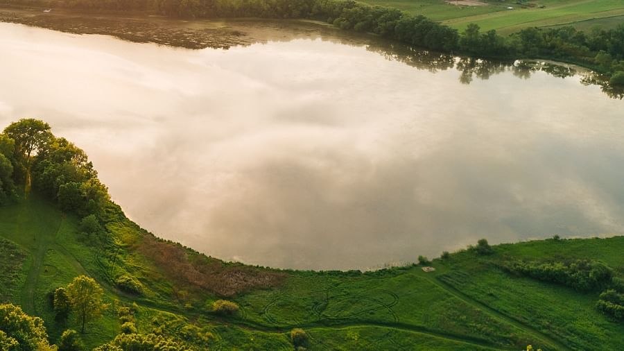 lake surrounded by green forest with the sun setting in the background