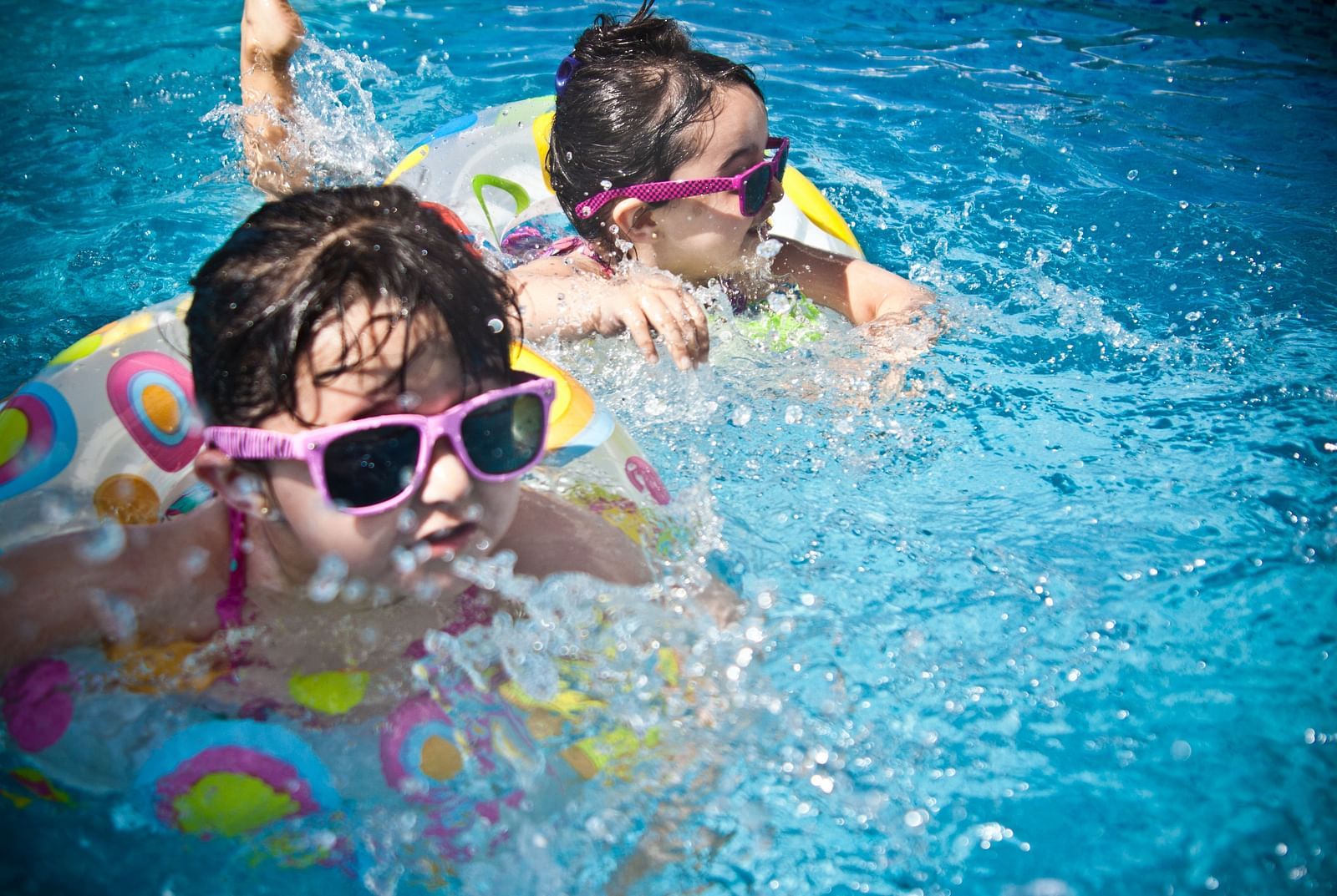 An image of two toddlers with sunglasses on in a swimming pool