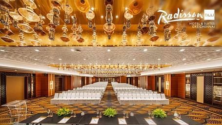 Elegant conference hall at Radisson Blu Hotel & Suites GRT Chennai with golden chandeliers and seating setup.