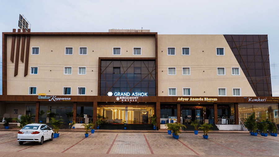 Facade of Grand Ashok, Thanjavur, with multiple windows and car parked parked in the front.