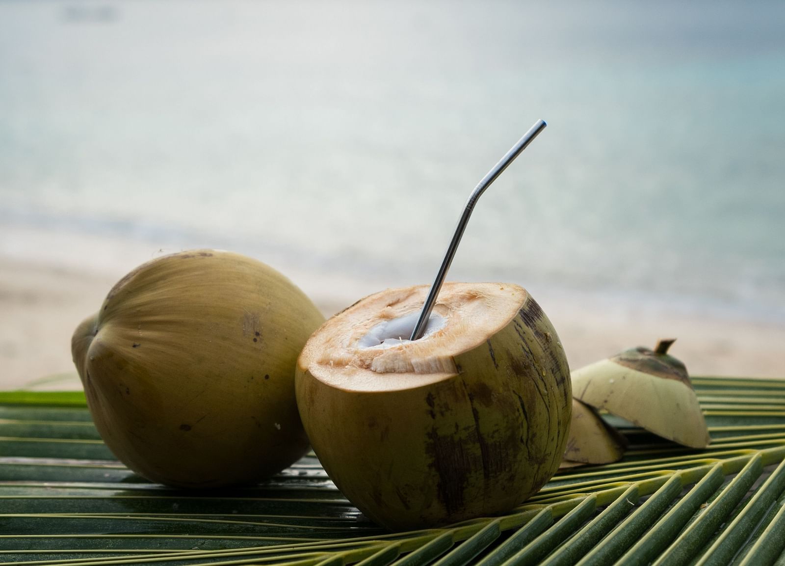 Two tender coconuts with straws placed on a green leaf outdoors at Flower Island Resort.