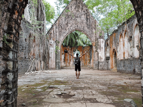A person standing inside the ruins of Ross Island with trees in the background