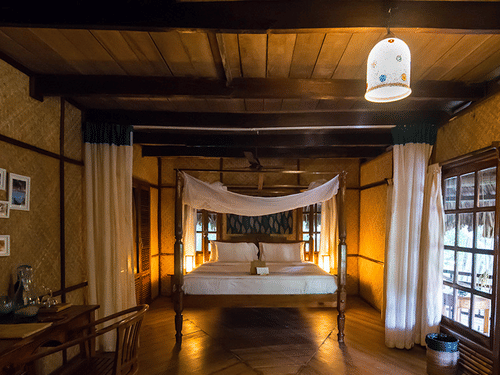 One of the Fan Cooled Duplex Cottages at Barefoot at Havelock featuring a plush bed with a canopy and a desk facing the wall with photos of beaches on it