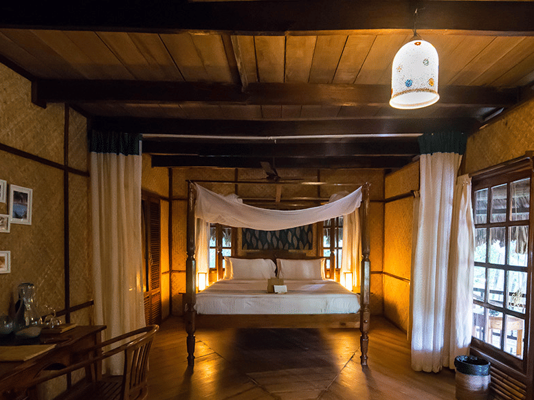 One of the Fan Cooled Duplex Cottages at Barefoot at Havelock featuring a plush bed with a canopy and a desk facing the wall with photos of beaches on it