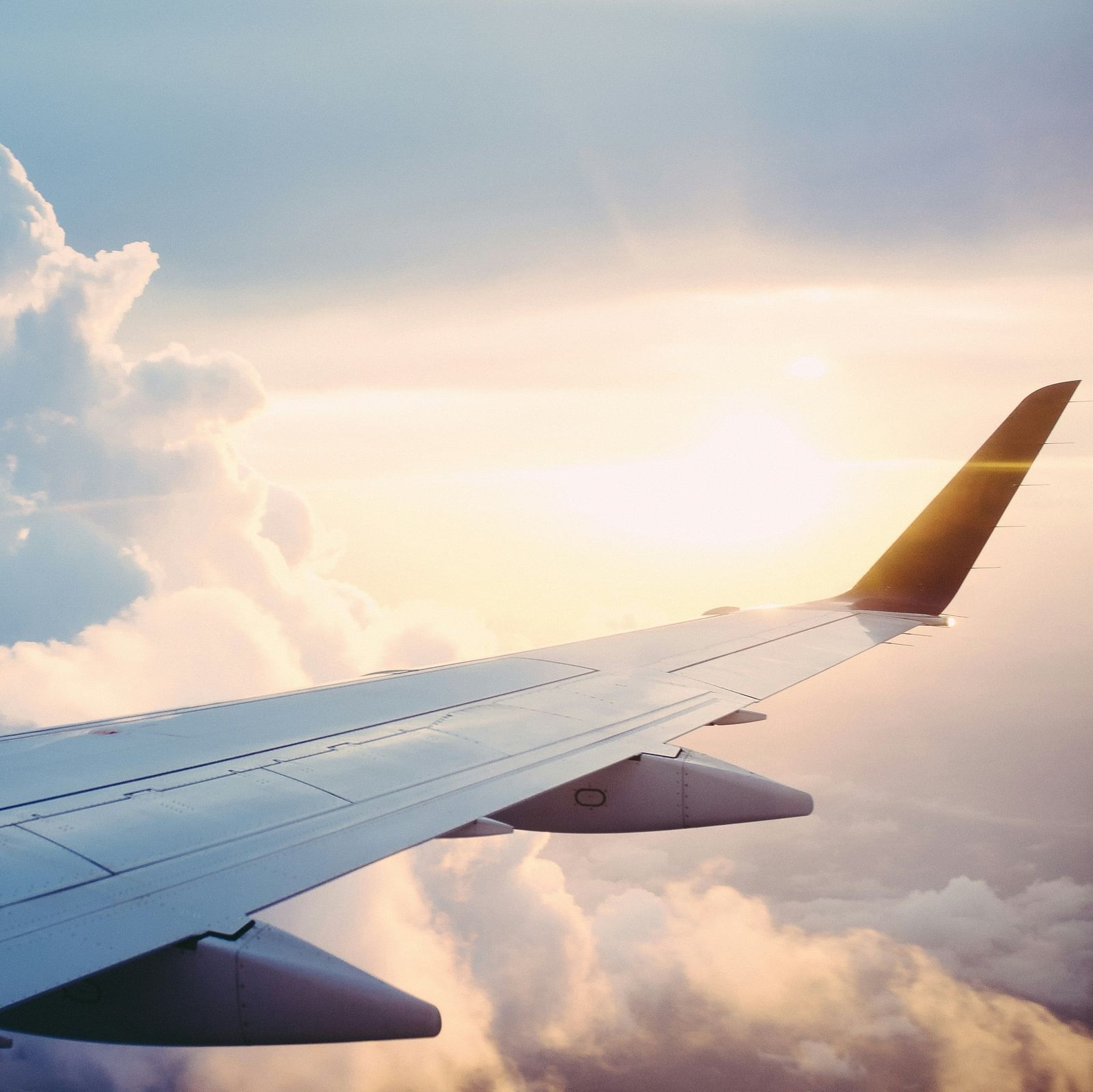 The image shows the wing of an aeroplane with clouds and sunlight in the background.