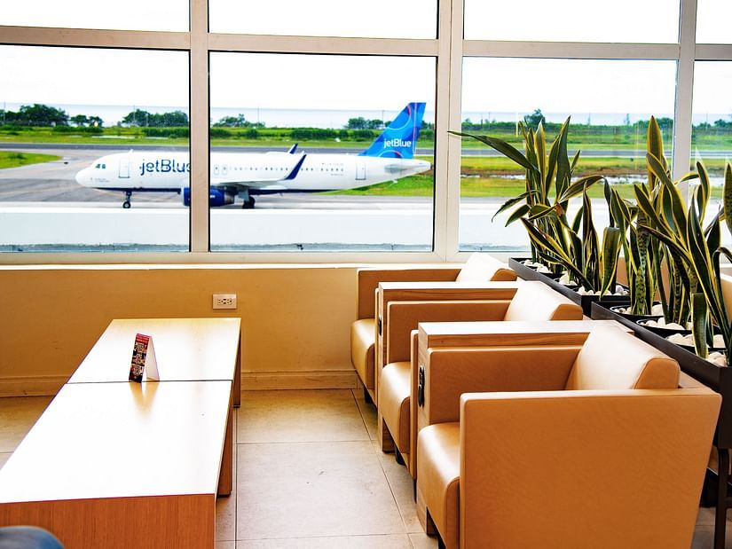 An image of a lounge featuring a sofa set, a table, and an expansive glass window over looking an aircraft on a runway