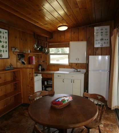 24The interior of a cabin showing a dining area with a round wooden table and chairs, adjacent to a kitchen area