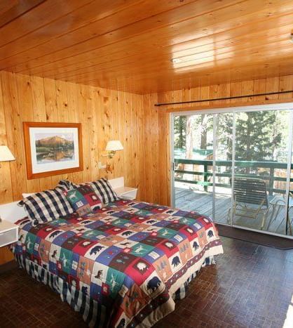 A warm, wood-paneled cabin interior revealing a bedroom with a patterned bedspread and an open doorway to another room | Snow shoe