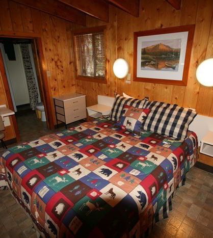 The interior of a cozy cabin bedroom featuring a patterned bedspread, wooden walls, and framed artwork | Red Squirrel