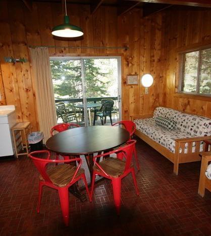 The interior of a spacious cabin features a living area with a sofa and armchairs, a dining area with a red table and chairs, and large windows offering a view of the outdoors | Gray Squirrel