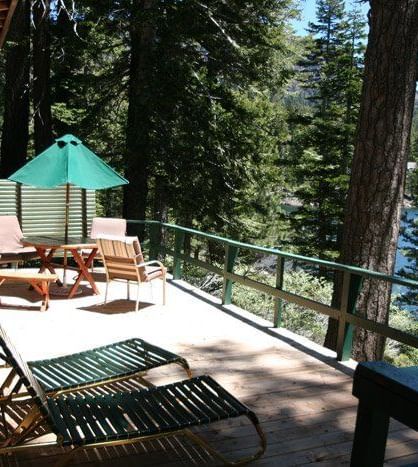 A wooden deck with an outdoor dining area and lounge chairs overlooks a river and lush green trees | Wolf