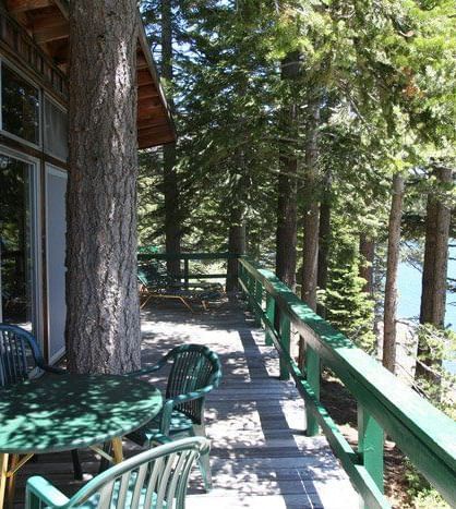 A cabin with a large deck overlooks a serene lake, surrounded by towering pine trees | Black Bear