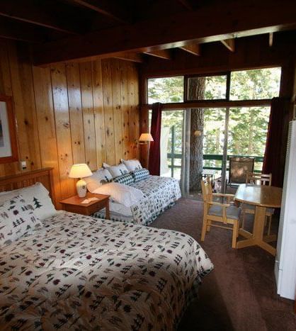 A cozy bedroom inside a cabin with a bed covered in a patterned comforter, wood-paneled walls, and large windows