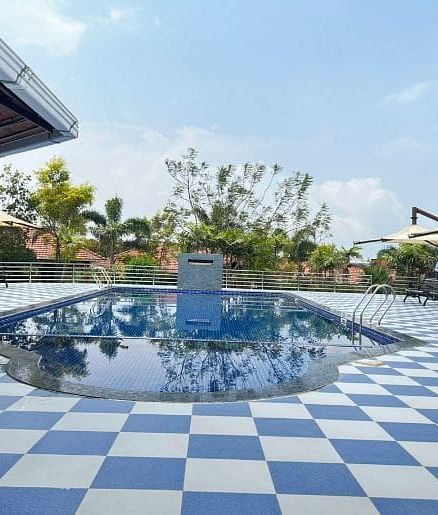 A serene pool area at Woodstock Resorts, Coorg featuring a checkered tile pattern and surrounding greenery.