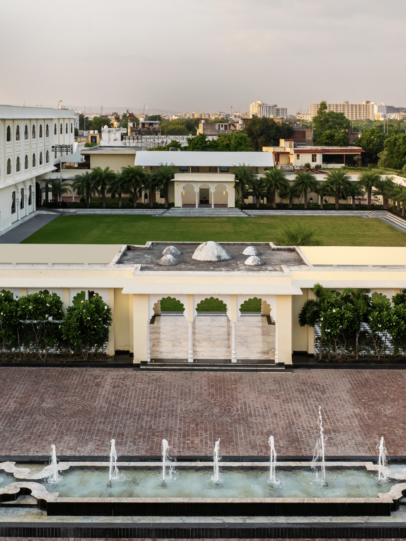 Facade of Beelwa Palace, Jaipur, featuring featuring elegant white architecture, landscaped courtyards, ornamental fountains and spacious grounds beneath an overcast evening sky