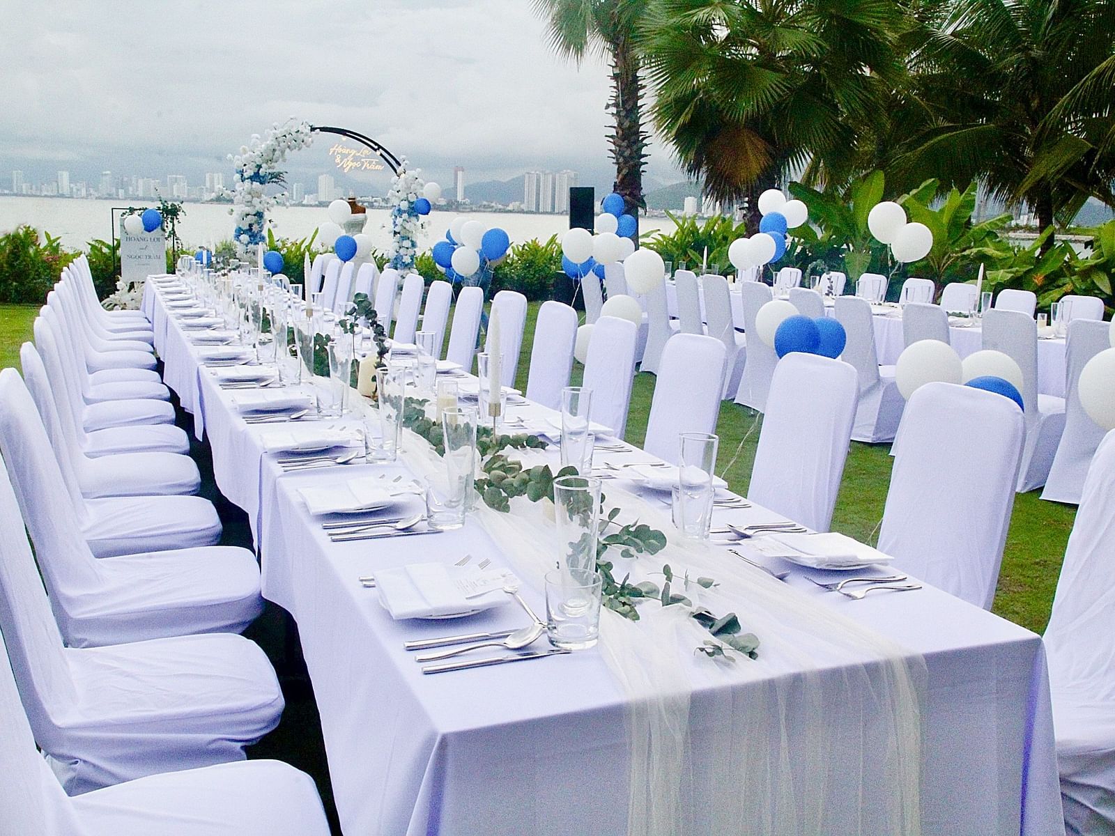 A long table with white chairs on a green lawn near the bay - Alibu Resort Nha Trang
