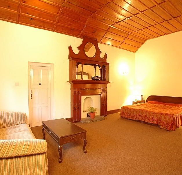 An image of a well lit Heritage Room with a bed , an almirah with mirror attached and has a few drawers, and on one corner there is a sofa with one centre table - The Earl s Court Nainital vrhc3h