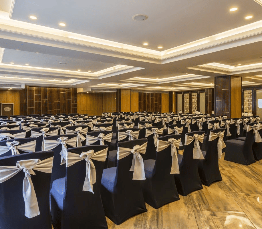 Spacious banquet hall with covered chairs, tables, and a large stage area - The Citrine