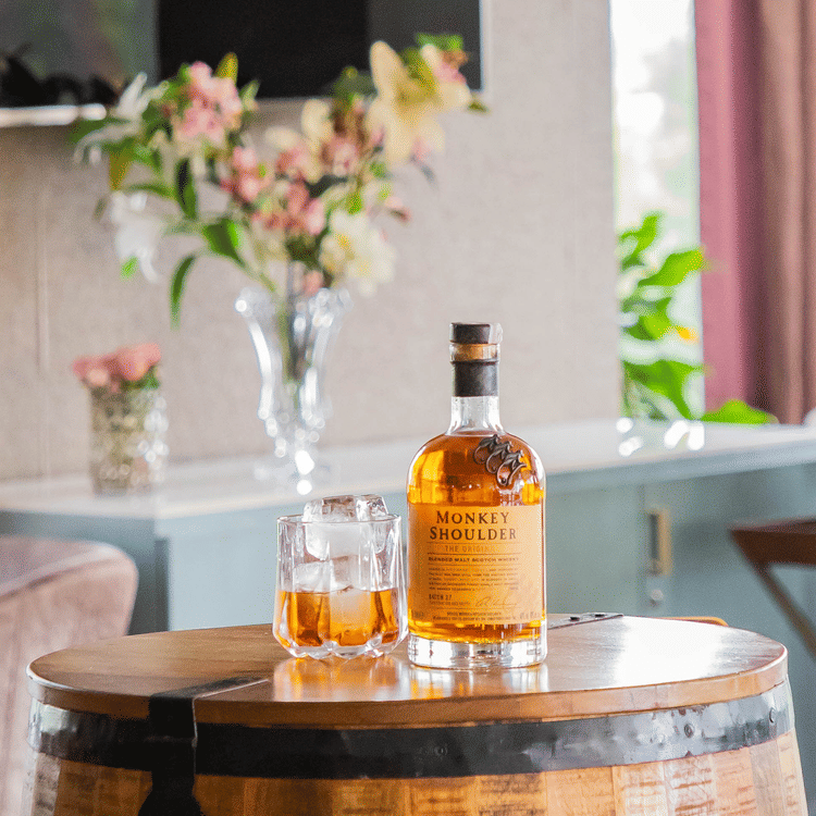 A close up shot of a dining table with a bottle, a vase and flowers kept on it - Karma Lakelands.