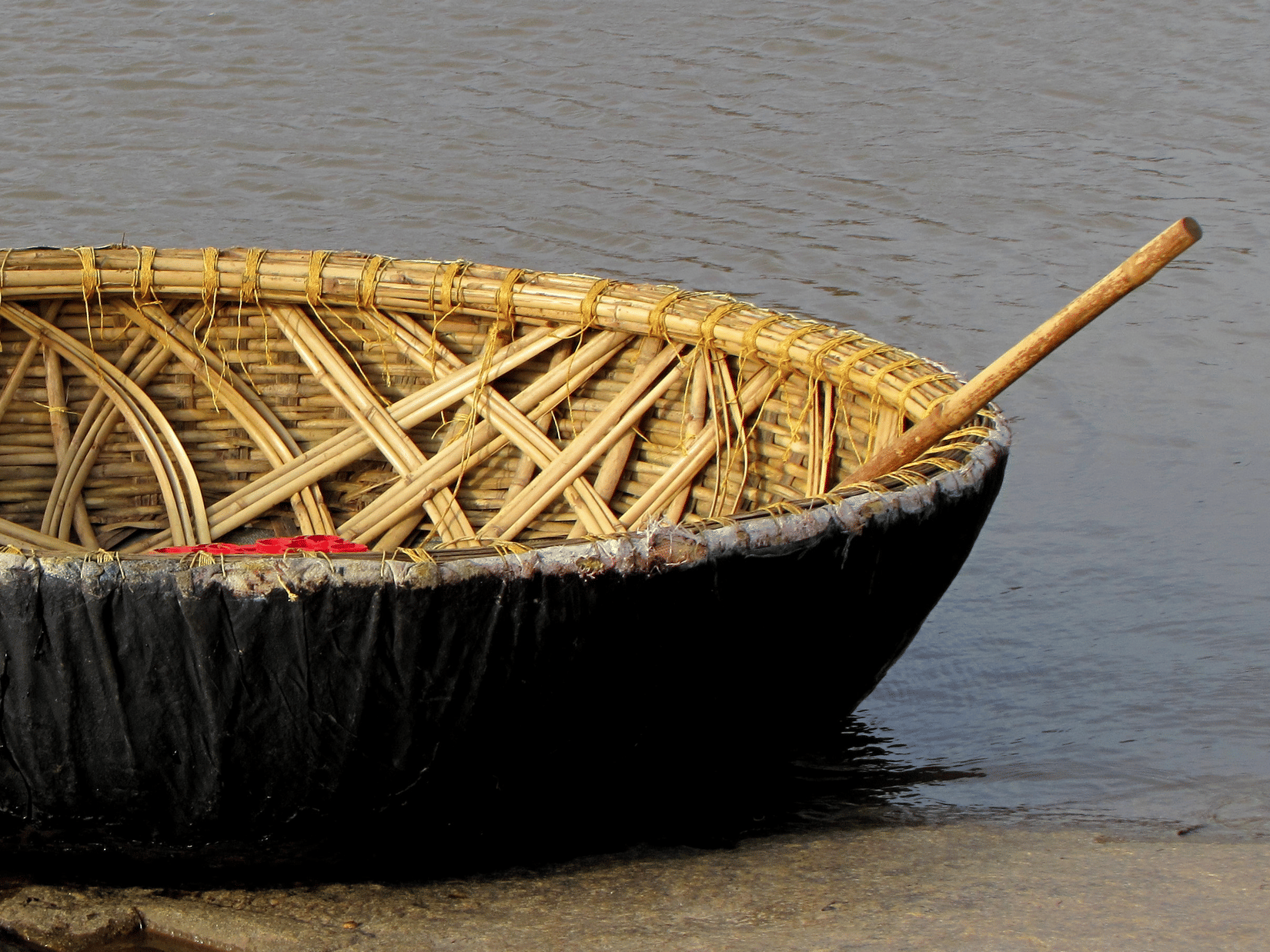 A close up of a Coracle boat with an oar kept inside it, floating on a waterbody near a step. These coracle rides provide opportunities to visit the many places to see in Kabini.