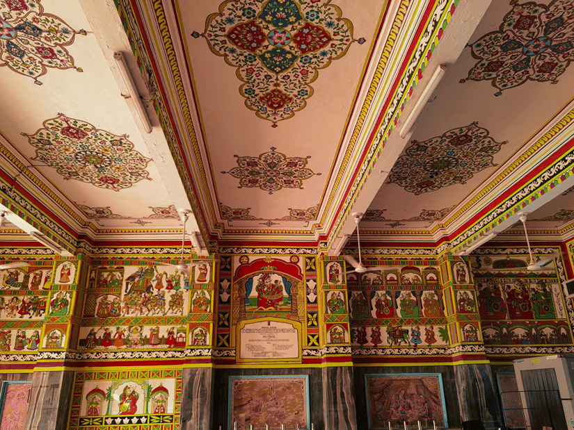 Elaborately painted Indian ceiling and walls adorned with intricate floral and historic frescoes.