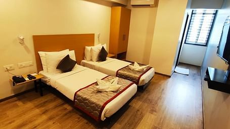 Hotel bedroom with two single beds, wooden furniture, and a view through the window - Lords Eco Inn Belagavi