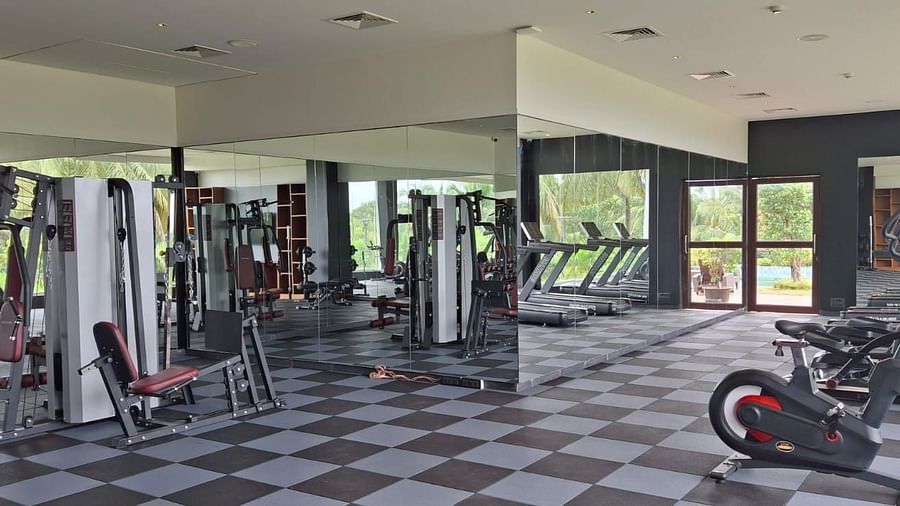 The fitness centre at Cloud9 Sarovar Premiere, Goa, features exercise machines with wall-mounted mirrors and a chess-patterned tile floor, creating an energising and stylish atmosphere