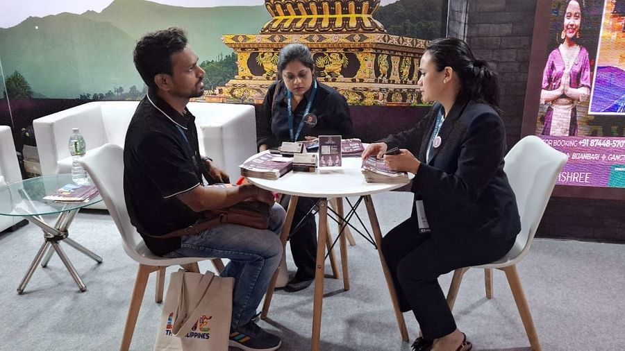 Three individuals engaged in a conversation at a round table with promotional materials for Sumi Yashshree Hotels displayed. 