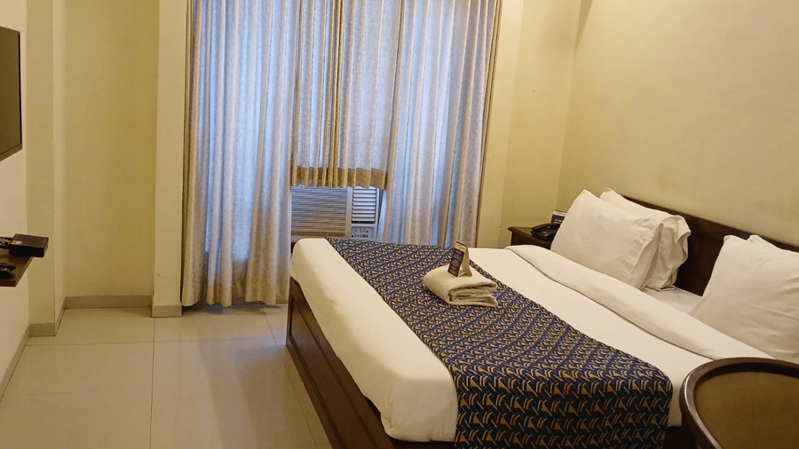 Deluxe Room at VITS Select, Bharuch featuring a double size bed, a flat TV screen on the wall, an AC, and a window with curtains drawn.
