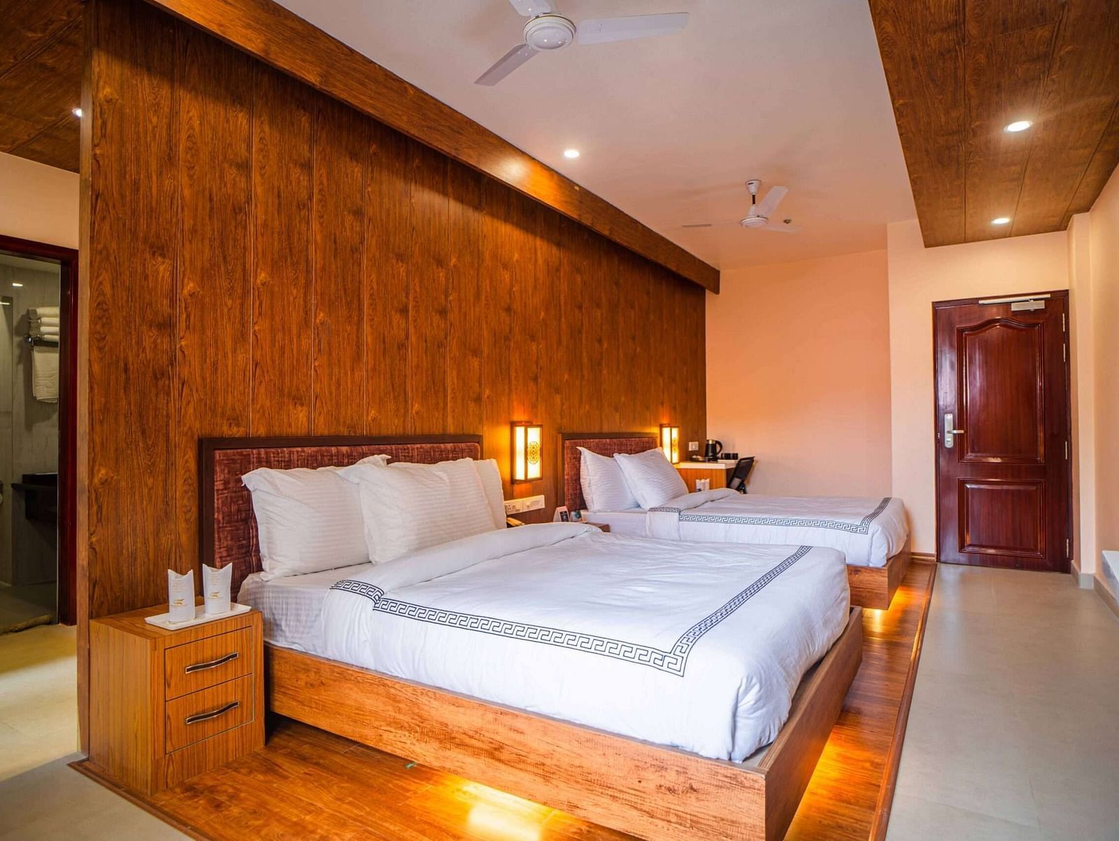 A comfortable hotel room at Mansha Palace features two beds, wooden accents, and a glimpse into the bathroom.