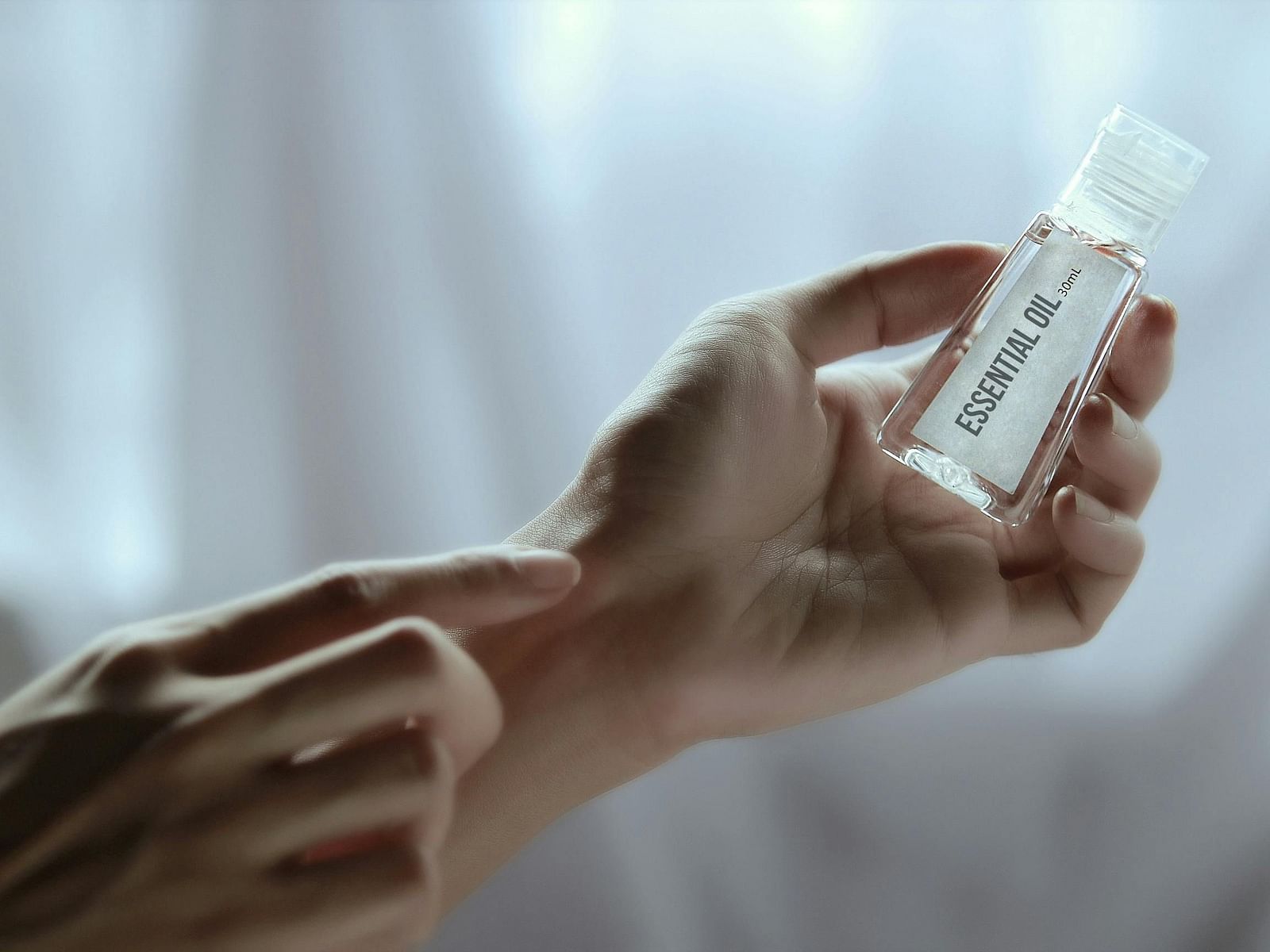  A person applies essential oil from a small clear bottle to their wrist.