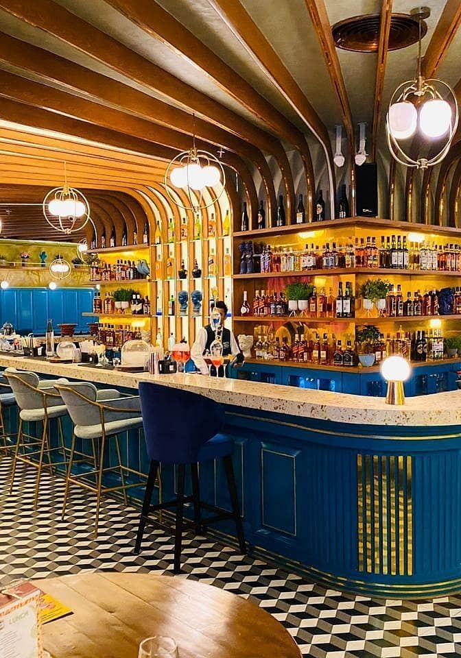 An image of a bar featuring a counter table, chairs, and a shelf where liquor items are placed - Themis Barbecue House, Panipat