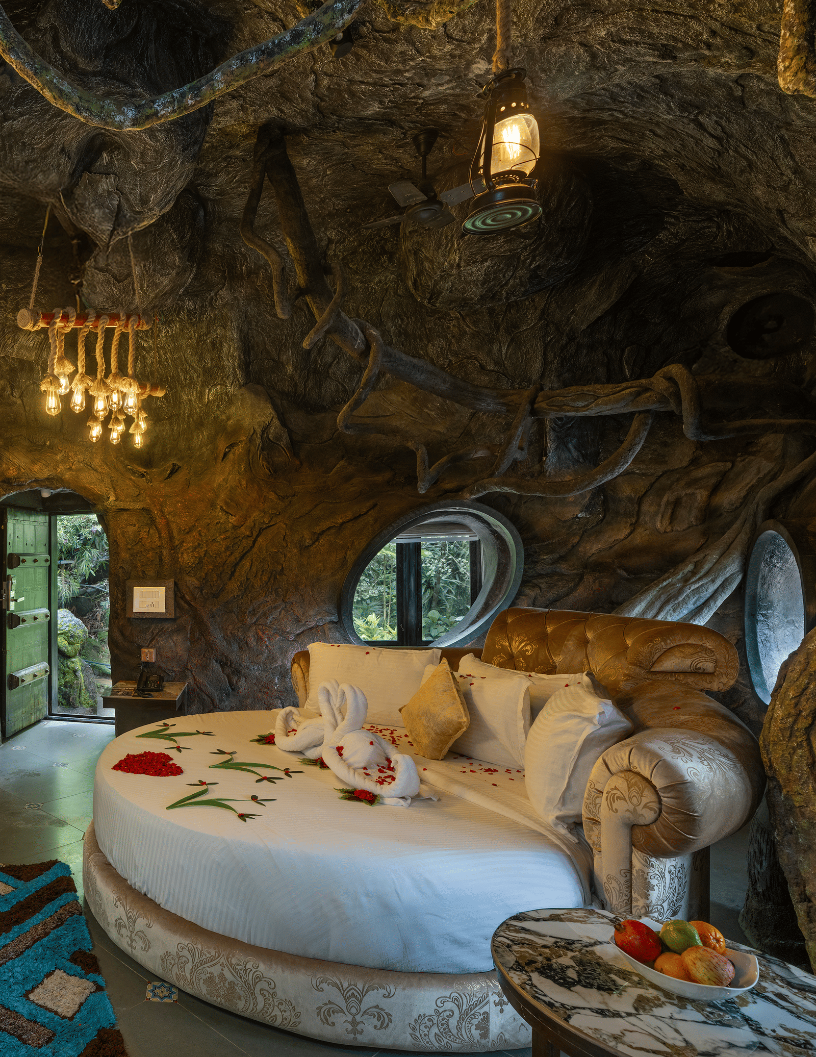The bedroom of the Cave Room at Parakkat Nature Hotel and Resorts, Munnar, featuring a large circular bed, decorative light fixtures, and walls designed to resemble natural rock formations.