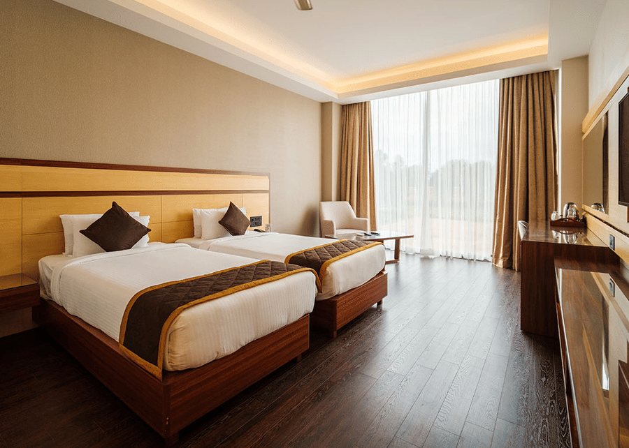 A spacious hotel room with twin beds, a wardrobe, a television, and a view of the outdoors. at The Residences at CSE, Banglore