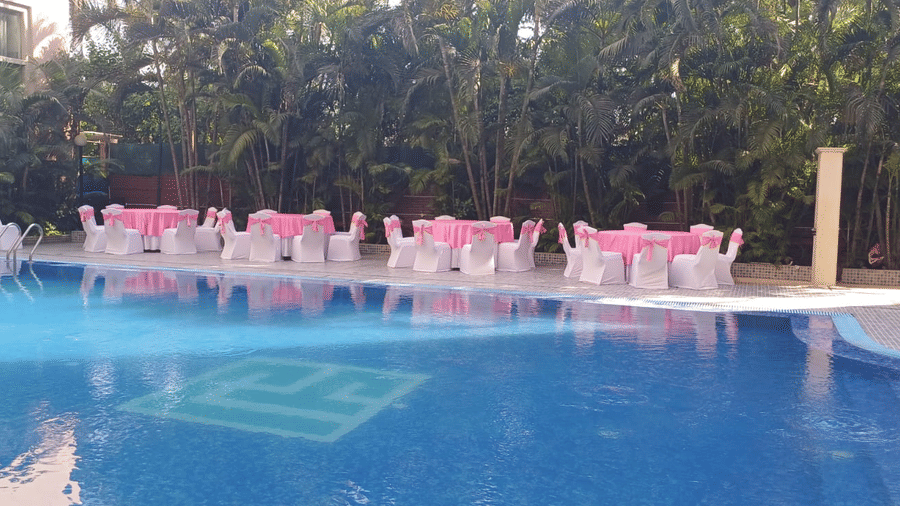 Poolside event setup at The Piccadily with pink and white chairs arranged along a blue swimming pool surrounded by lush greenery.