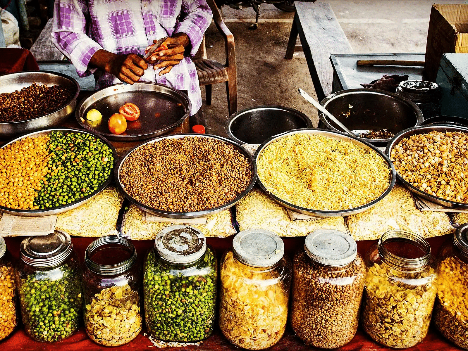 Vibrant street food market showcasing jars and trays of colourful Indian snacks.
