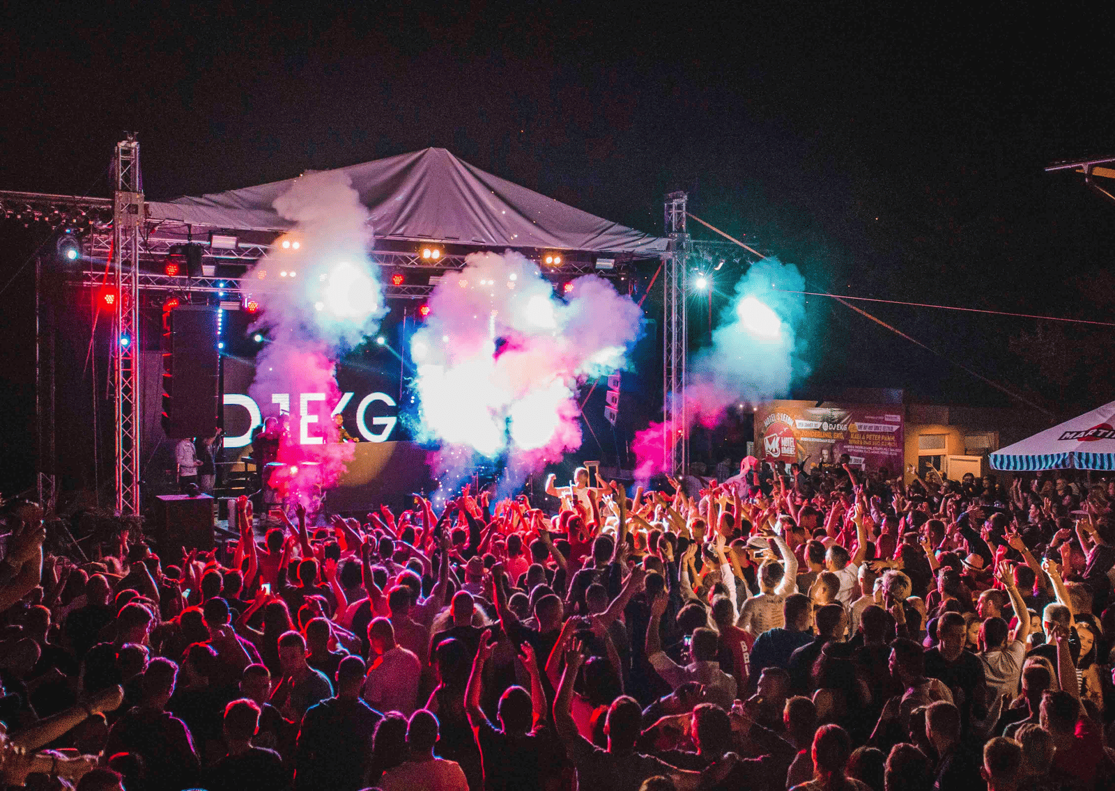 A crowd enjoying an outdoor concert with colourful lights and smoke effects