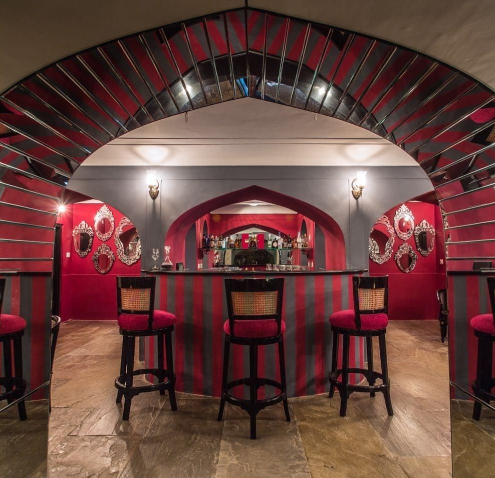 A bar area at Royal Heritage Haveli featuring red walls, arched architectural details, and bar stools.