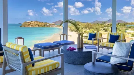 A spacious living area with modern furniture, featuring expansive windows overlooking a vibrant blue ocean and a distant island.